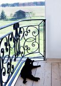 Eine schwarze Katze putzt sich auf der Galerie mit Panoramablick über die ländliche Umgebung