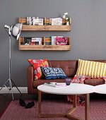 Home-made, wall-mounted rustic shelves above modern leather sofa with colourful cushions