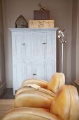 Shabby chic wardrobe behind tasteful leather armchairs