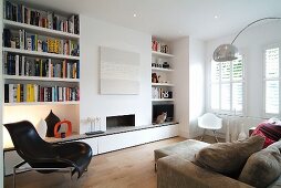Modern living room with integrated bookcases either side of open fireplace and classic chairs