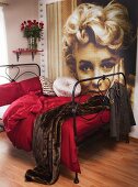 Schwarzes Metallbett mit weinroter Bettwäsche und Pelz-Tagesdecke; an der Wand ein großes Marilyn Monroe Portrait