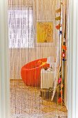 View through airy fringe curtain to colorful corner of room with orange armchair