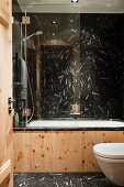 View into extravagant chalet bathroom with black and white stone tiles on floor and walls and bathtub with pine wood cladding