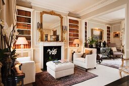 Armchairs with linen upholstery and button tufted ottoman on Oriental rug; French, gilt-framed mirror on mantelpiece above fireplace