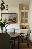 Armchairs with smoky blue linen upholstery and curved wooden legs at round Victorian table with central pedestal