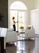 Sitting area with cubic leather armchairs; behind, a lady in an open, arch top French door