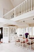 White, country-house-style open-plan dining area with gallery and white-painted wooden furniture