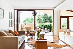 Sofa and simple, wooden coffee table on glossy wooden floor with animal-skin rug in front of open terrace door
