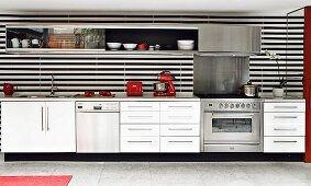 White, modern kitchen counter with black and white striped rear wall, mirrored wall at one end and red kitchen appliances