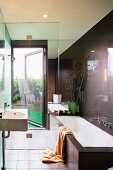 Designer bathroom in dark brown - wash basin and bathtub in front of a glass shower stall with access to the terriace