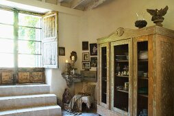 Crockery in vintage, glass-fronted cupboard next to terrace door in interior of simple country house