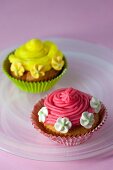 Cupcakes mit roter und gelber Zuckercreme und Zuckerblüten verziert