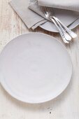 A simple white porcelain plate with forks and napkins next to it