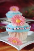 Hellblaue Cupcakes mit rosa Blüten und Zuckerperlen