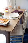 Savoury bake, salad and single place setting with white crockery on simple wooden table and kitchen chair