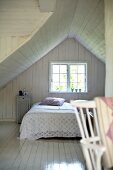 White, wood-clad attic bedroom in simple wooden house