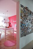 View from hallway with large collection of photos on wall into pink dining room with white dining table and pink rug