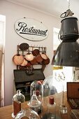 Old restaurant sign above collection of shiny copper pans hanging on wall rack; several bell jars in foreground