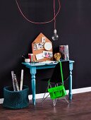 Black shell chair at console table painted light blue against dark blue wall and simple pendant lamp with light bulb