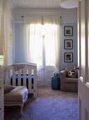 View through open door of vintage cot and French windows with gathered curtains in traditional interior