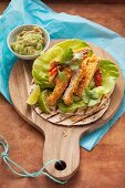 Strips of schnitzel in a nacho crumb coating, guacamole and tortillas