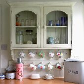 Floral patterns on thermos and cups hanging from rack below old, wall-mounted cabinet in vintage kitchen