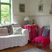Patchwork, floral gemusterte Decken und Kissen in einer Wohnraumecke mit halbhoher Holzvertäfelung