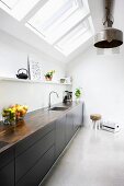 Monolithic kitchen counter with black fronts below strip of skylights and metal, industrial-style pendant lamps