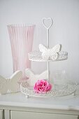 weiße Deko-Schmetterlinge, eine rosa Rose und ein Wasserglas auf einer Etagere