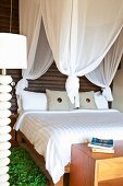 Doppelbett unter weißem Baldachin vor dunkler Holzwand und grünem Bettvorleger