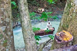View of woman lying on massage table in stream and masseuse seen through trees