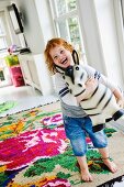 Laughing child with toy animal on colourful kilim rug