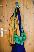 Abgebeizte Vintage Tür mit verknautschter Tasche und Kleidung an Metallhaken