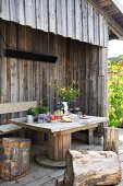 Tisch mit Bank und Baumstamm-Hockern auf der Terrasse einer Holzhütte