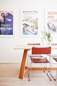 Delicate metal chairs with leather seats and backs around wooden table in front of framed posters on wall