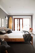 Simple double bed with wooden frame in room painted dark grey with large French window