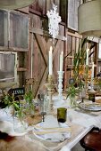Table set festively with lit candles and wild flowers in jars against rustic wooden wall