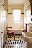 View through open door of antique wooden chair and patterned tiled floor in vintage bathroom
