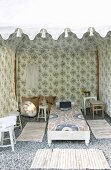 View into tent-like pavilion made from floral fabric with rugs surrounding daybed on gravel floor