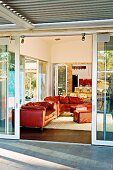 Blick von Terrasse durch offene Schiebetür auf rote Ledercouchgarnitur im Wohnzimmer