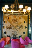 Enormous, floor-to-ceiling clock with phases of moon and zodiac applied to wall; armchairs with pink upholstery in foreground