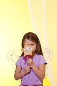 A Little Girl Wearing Fairy Wings Holding a Star Shaped Cake Pop with Colored Sprinkles