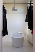 Purist bathroom with free-standing bathtub and industrial-style pendant lamp; dark clothing on clothes hangers hung on metal rod