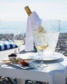Gedeckter Tisch am Strand mit Vorspeisen, Weissweingläsern und Weinflasche im Kühler