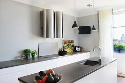 Free-standing kitchen island with sunken sink below pendant lamp and kitchen counter along wall with futuristic extractor hood
