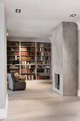 Minimalist interior with open-plan fireplace in concrete wall opposite armchair in front of fitted bookshelves