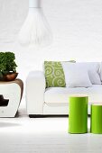 Green-varnished, cylindrical side tables in front of white sofa and designer pendant lamp with white slatted lampshade