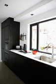 Kitchen counter with black fitted cupboards against wall with window