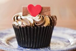 A cupcake topped with gold icing and a heart