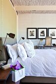 Double bed with upholstered headboard and scatter cushions flanked by retro metal table lamps on bedside tables in modern bedroom